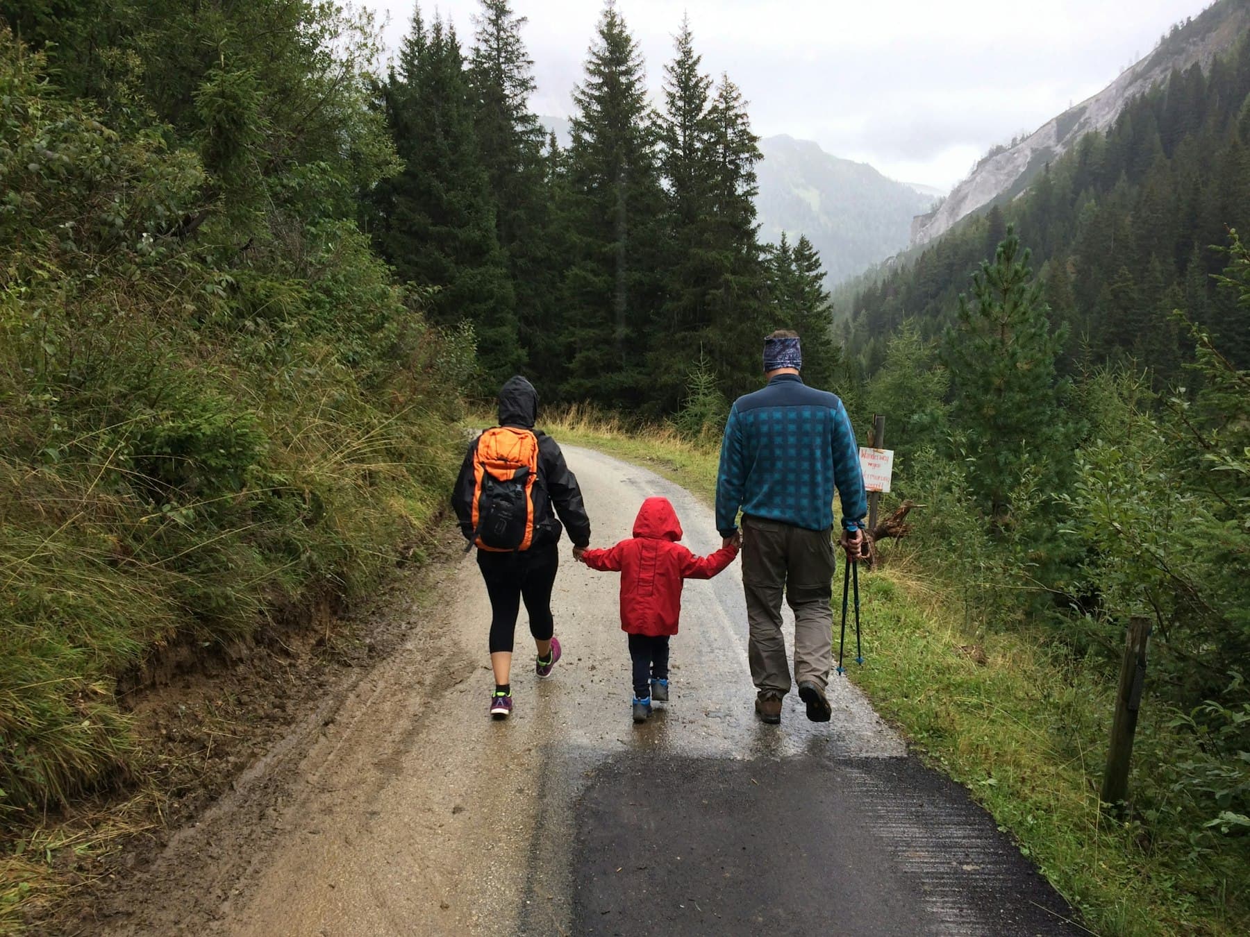 A family walking together along a quiet dirt road, surrounded by trees