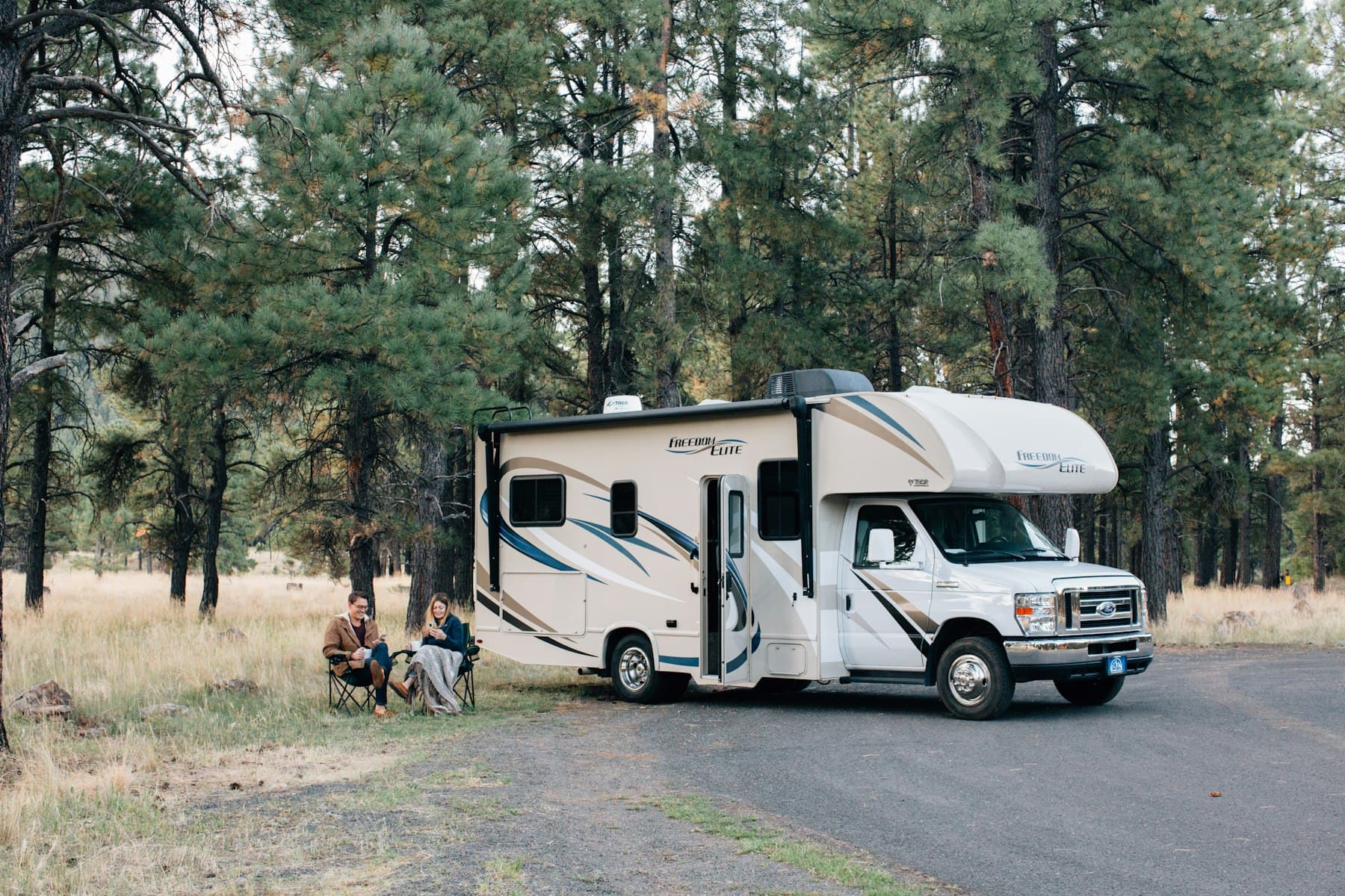 Two people standing beside a white RV trailer on a bright afternoon