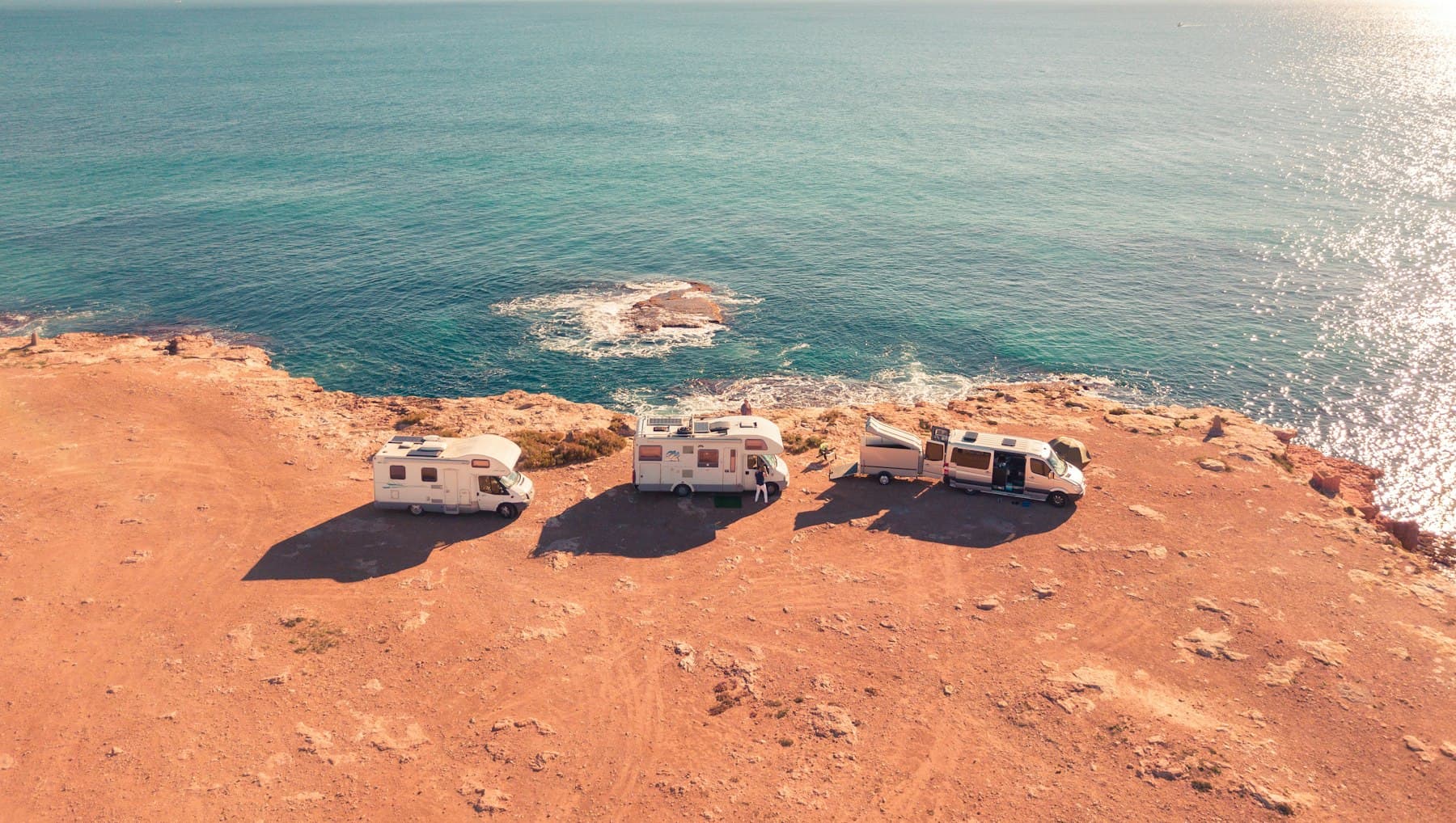Three white RVs parked together near the sea on a bright afternoon